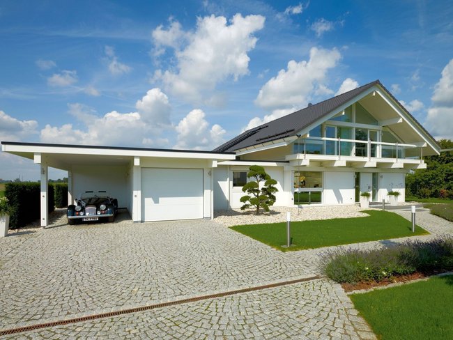 Fachwerkhaus HUF HAUS ART 4 in moderner Architektur Fachwerkhaus mit Carport und grüner Umgebung unter blauem Himmel
