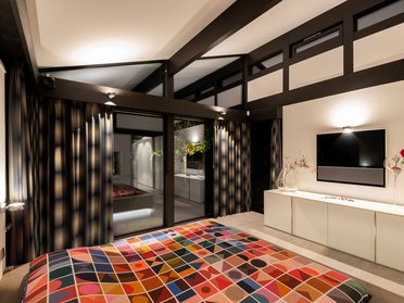Schlafzimmer mit buntem Bett und großen Glasfenstern im Bungalow
