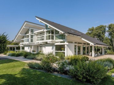 Helles Fachwerkhaus umgeben von Bäumen und Gartenlandschaft