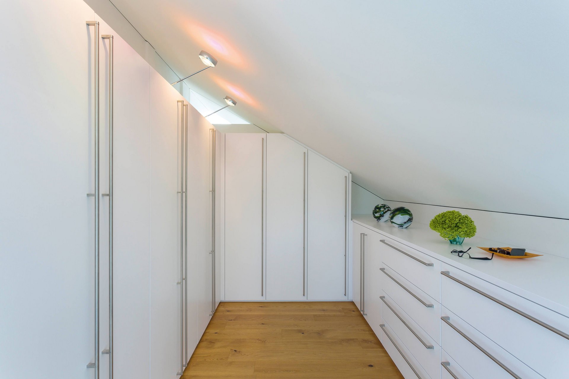 Helles Dachzimmer mit weißen Schränken und Holzfußboden