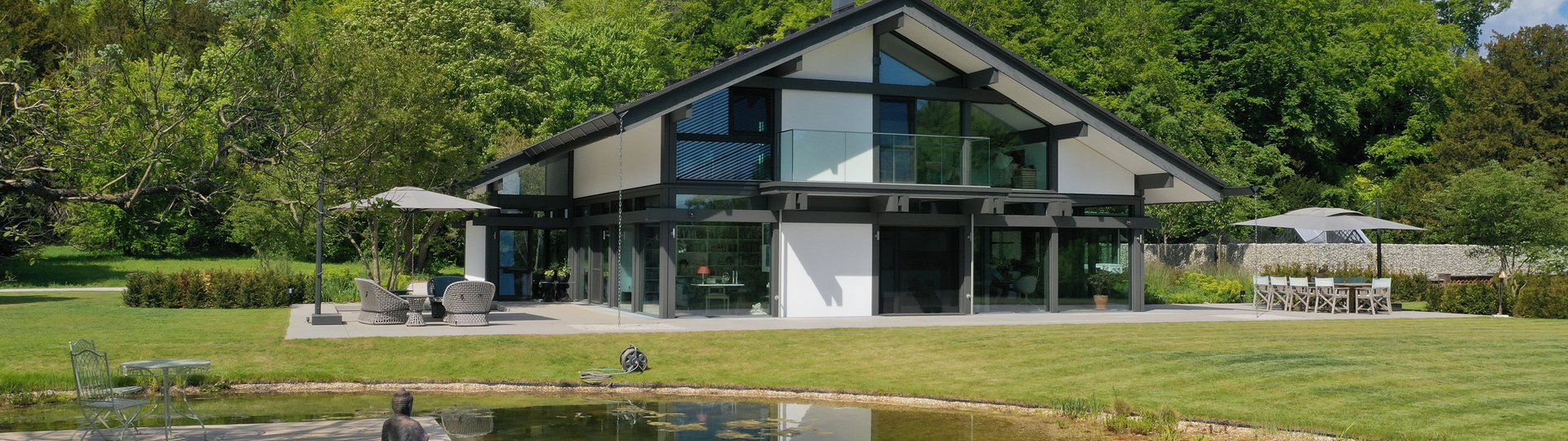 Modernes Gebäude mit grünem Landschaftsdesign Helles, modernes Haus umgeben von Bäumen und einem Teich