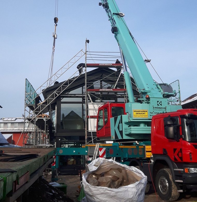 Baukran hebt Teile über einer Baustelle mit Fahrzeugen und Materialien.