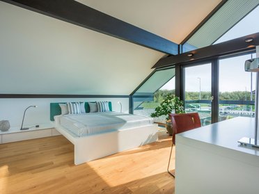 Helles Schlafzimmer mit Holzfußboden, großem Fenster und stilvoller Dekoration