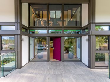 Eingangsbereich eines modernen Gebäudes mit Glasfächen und pinker Tür