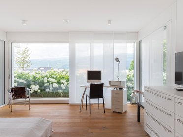 Helles Schlafzimmer mit großen Fenstern und minimalistischer Einrichtung