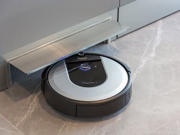 Roboterstaubsauger unter der Küchenzeile Ein Roboterstaubsauger ruht unter einer Küchenzeile auf einem modernen Boden