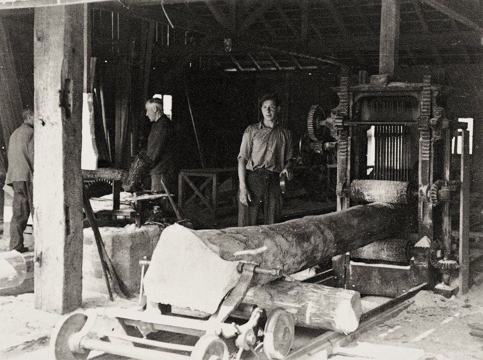 Historische Holzverarbeitung in einer Sägewerkshalle Arbeiter in einem Sägewerk mit Holzsäge und Maschinen