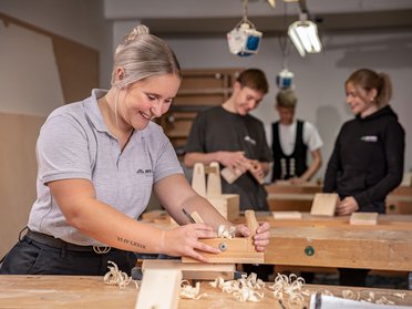 Woman using a hand plane in a woodworking workshop Group of people engaged in woodworking activities in a workshop