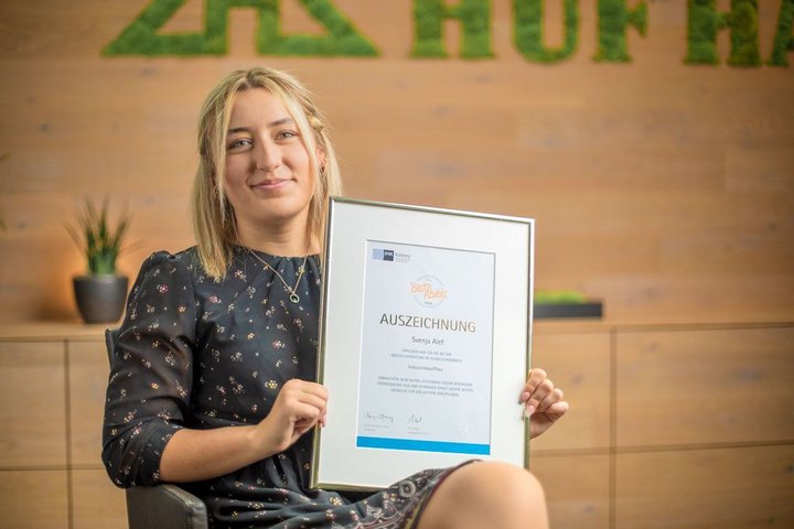 Eine Frau hält stolz ein Auszeichnung-Zertifikat in einer modernen Büroatmosphäre