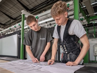 Junge Männer arbeiten gemeinsam an technischen Plänen Zwei junge Männer betrachten und besprechen technische Zeichnungen in einem modernen Arbeitsumfeld.