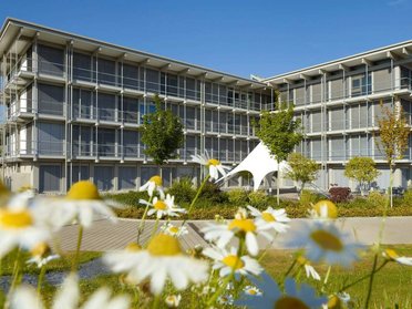 Bürogebäude HUF umgeben von Blumen und blauem Himmel