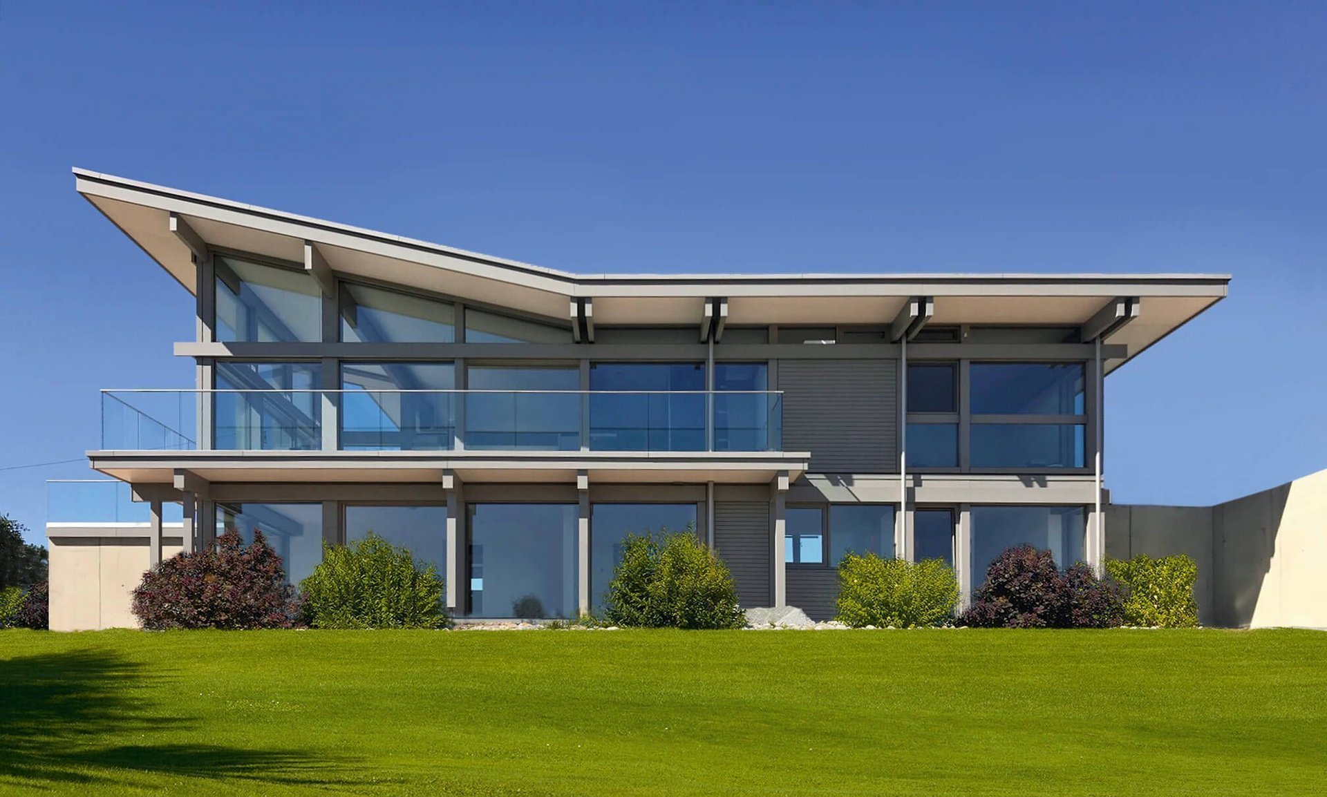 Modernes Haus mit Glasfassade und großzügiger Rasenfläche Ein stilvolles modernes Haus mit Glasfenstern und Pflegerasen.