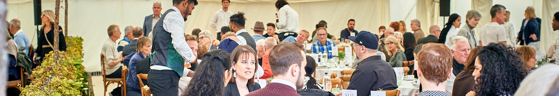 Elegant outdoor dining event under a marquee Guests enjoying a meal at round tables in a large tent