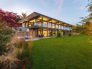Transparente Architektur des HUF HAUS mit Flachdach und grüner Umgebung