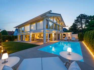 Ansicht eines modernen HUF Hauses mit beleuchtetem Garten und Pool