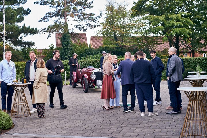 People socializing outdoors with a classic car and trees around