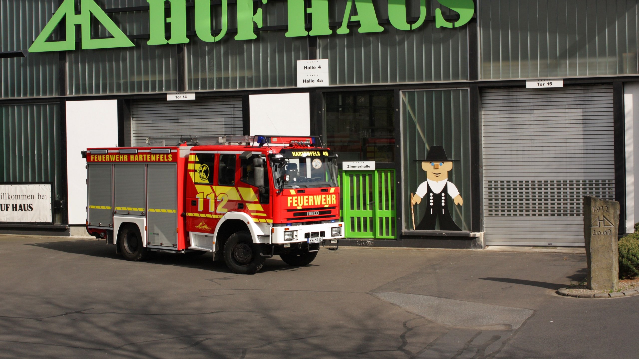 Rotes Feuerwehrfahrzeug steht vor HUF HAUS mit grüner Fassade