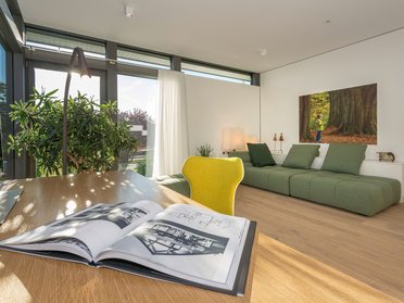 Ein heller Raum mit Sofa, Tisch und großen Fenstern.