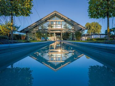 Transparentes Fachwerkhaus mit Garten und Panorama Fachwerkhaus aus Holz und Glas mit Bachlauf und Spiegelung im Wasser