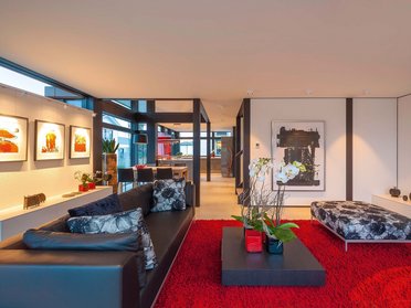 HUF Haus modum 810 Musterhaus Wuppertal 15 Ein eleganter Wohnbereich mit schwarzem Sofa und rotem Teppich.