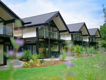 Moderne Holzhäuser mit Glasveranden in der Natur Reihenhäuser mit grünem Garten und blühenden Pflanzen