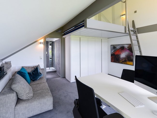 Luftiger Raum mit grauem Sofa, Schreibtisch und Treppe zur Empore