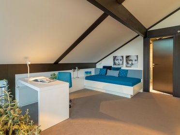 Helles Zimmer mit Sitzgelegenheit, Schreibtisch und Bildern an der Wand