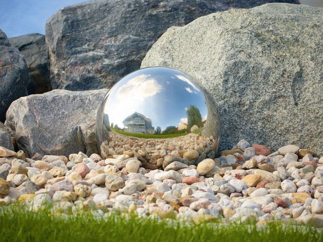 Reflektierende Kugel zwischen Steinen und Kieselsteinen Metallische Kugel spiegelt Umgebung zwischen Felsen und Kieselsteinen wider