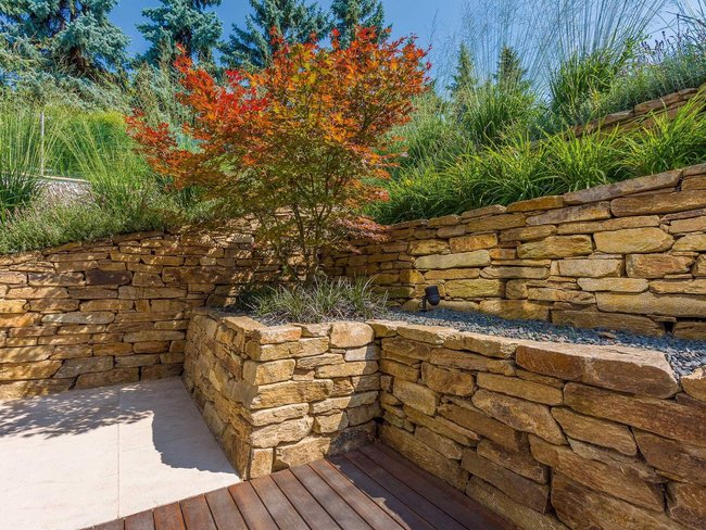 Gestaltung mit Natursteinmauer, Pflanzen und Holzbelag im Garten