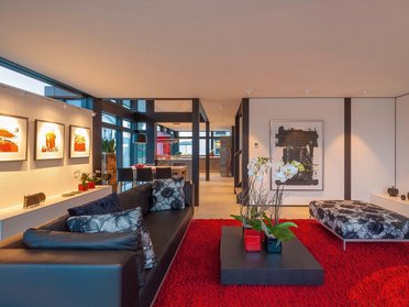 HUF Haus modum 810 Musterhaus Wuppertal 14 Helles Wohnzimmer mit Kunstwerken, Pflanzen und rotem Teppich