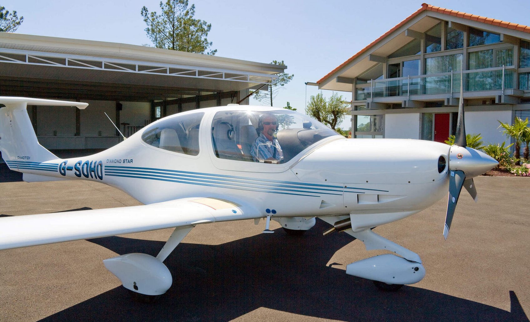Flugzeug vor modernem Haus und Hangar, sonniger Tag