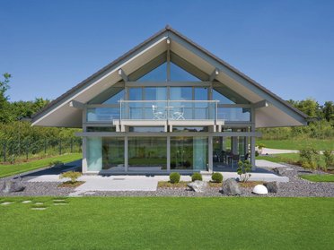 Haus mit Glasfront und Gartenlandschaft unter blauem Himmel