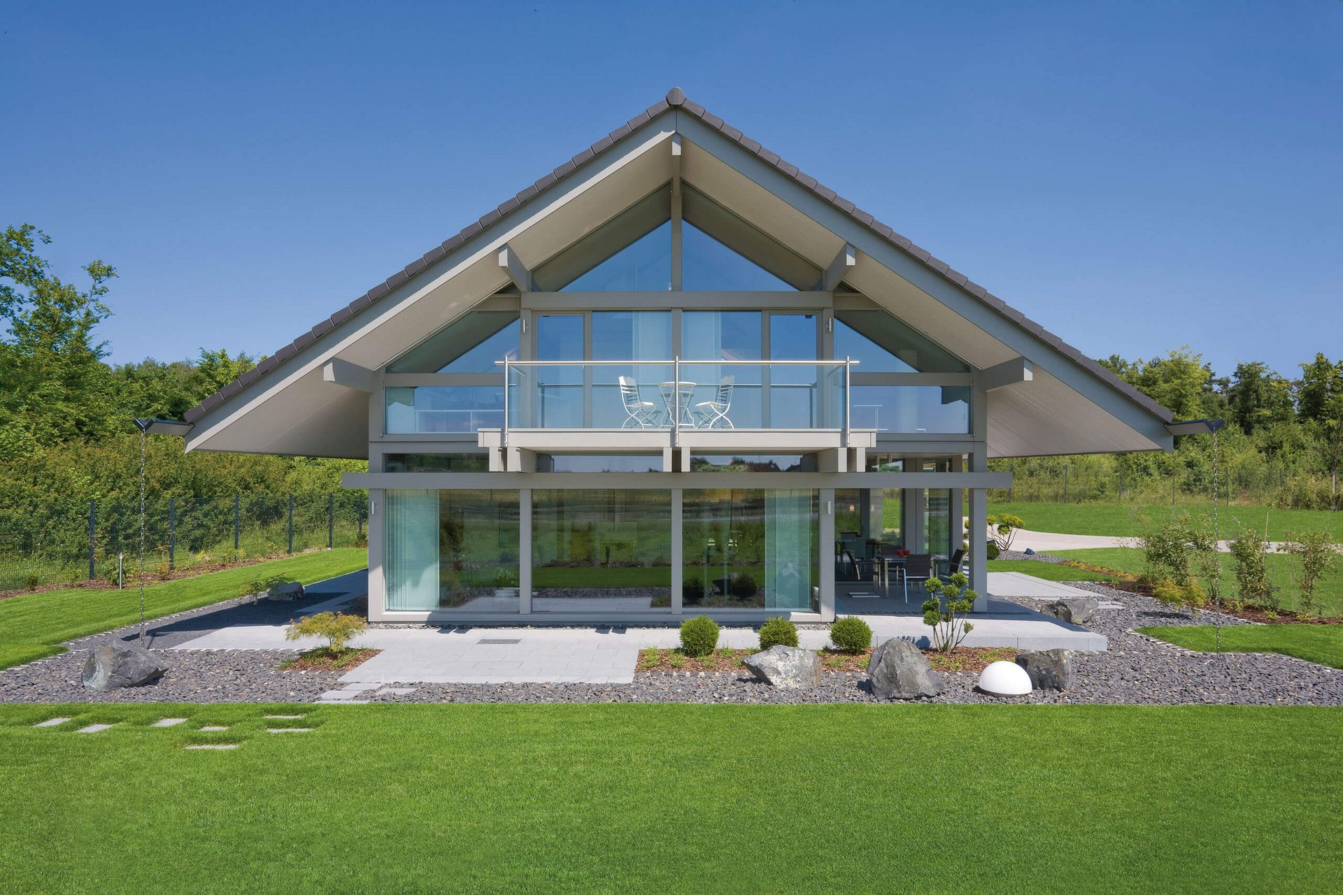 Haus mit Glasfront und Gartenlandschaft unter blauem Himmel