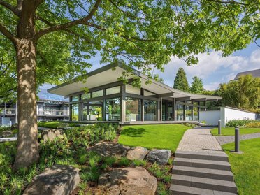 Moderne Architektur in einer grünen Umgebung Ein zeitgenössisches Gebäude umgeben von Bäumen und Gartenlandschaft
