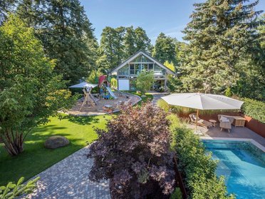 HUF Haus mit Anbau und Poolhaus in grüner Umgebung Blick auf HUF Haus mit Anbau, Poolhaus und Spielbereich im Garten