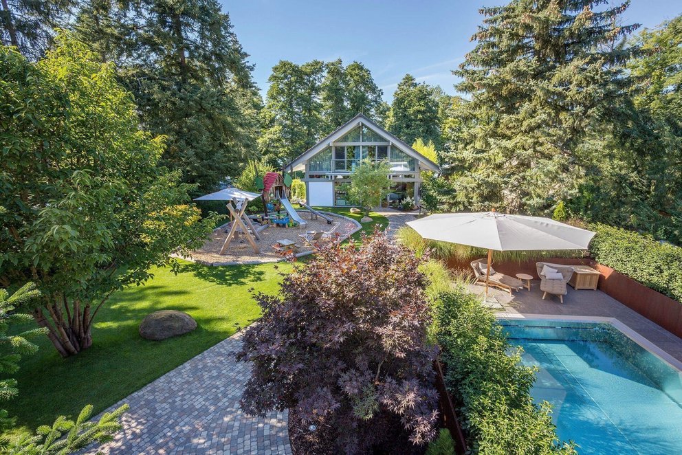 Blick auf HUF Haus mit Anbau, Poolhaus und Spielbereich im Garten