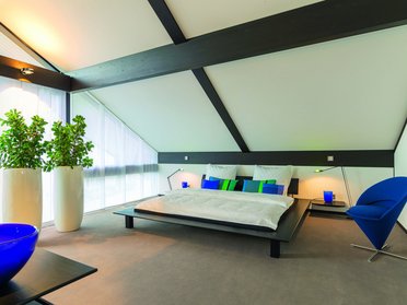 Schlafzimmer mit großen Fenstern, Pflanzen und stilvollen Dekorationselementen