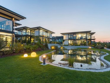Architektenhaus mit Glasfassade und beleuchtetem Teich bei Sonnenuntergang