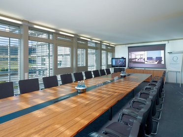 Heller Konferenzraum mit langer Holztafel und moderner Technik