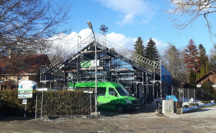 Bauarbeiten an einem modernen Gebäude mit Gerüst Unvollendetes Gebäude mit Baugerüst und einem grünen Van