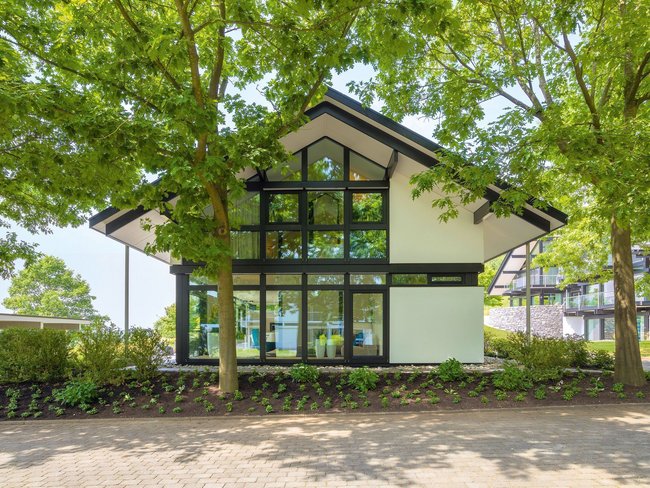 Ein modernes Gebäude mit großen Fenstern, umgeben von Bäumen und Grünflächen.