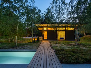 Modernes HUF Bungalow mit Pool und Garten Stilvolles Bungalow mit Holzterasse, umgeben von Bäumen und Pool