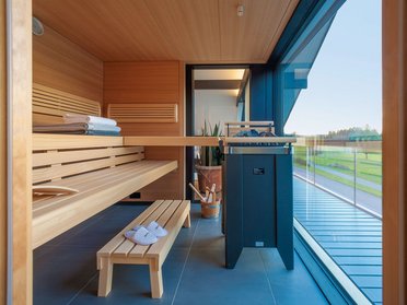 Innenansicht einer Sauna mit Holzbank, Handtüchern und Blick ins Freie
