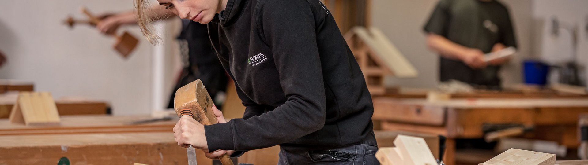 Junge Frau beim Holzarbeiten in einer Werkstatt Eine Frau arbeitet konzentriert mit einem Meißel an Holz in einer Tischlerei