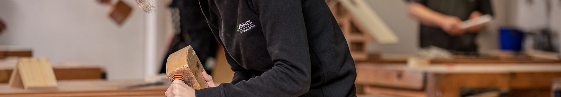 Junge Frau beim Holzarbeiten in einer Werkstatt Eine Frau arbeitet konzentriert mit einem Meißel an Holz in einer Tischlerei