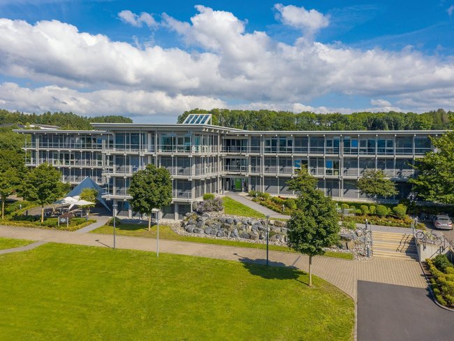 Ansicht des HUF Bürogebäudes mit Parkanlage und Wolken