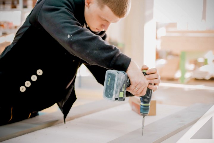 Handwerker bei der Arbeit mit Bohrmaschine Ein Handwerker bohrt in ein Holzstück in einer Werkstatt