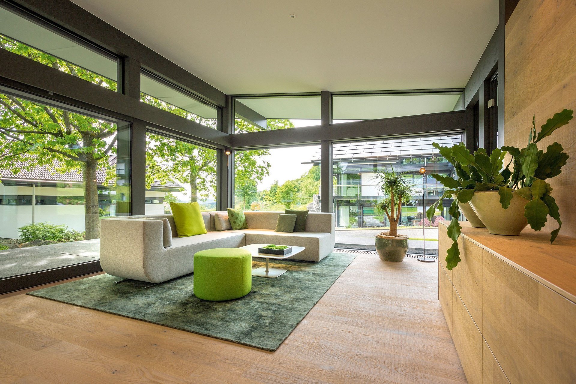Modernes Wohnzimmer mit großen Fenstern und Grünflächen Helles Wohnzimmer mit modernem Möbeldesign und Pflanzen