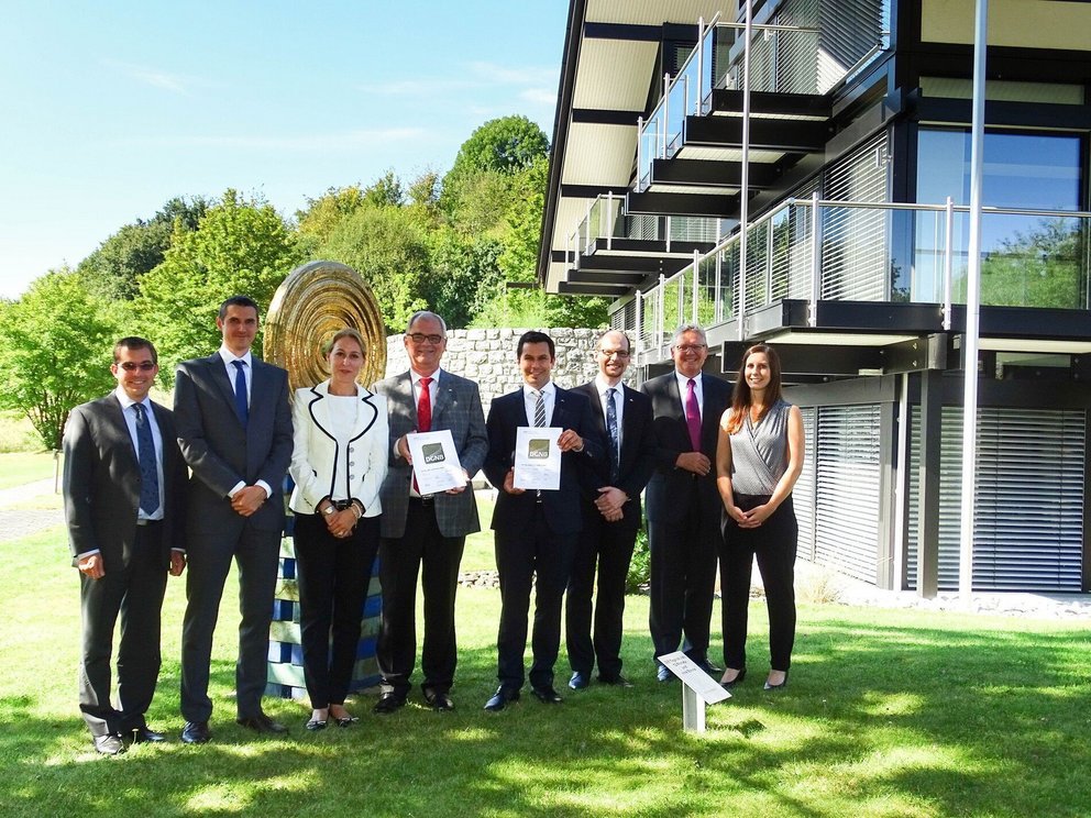 Gruppenfoto vor modernem Gebäude mit Auszeichnungen Personen präsentieren Urkunden vor einem modernen Gebäude im Freien