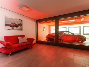 Bungalow mit rotem Sofa und Porsche in der Glasbox